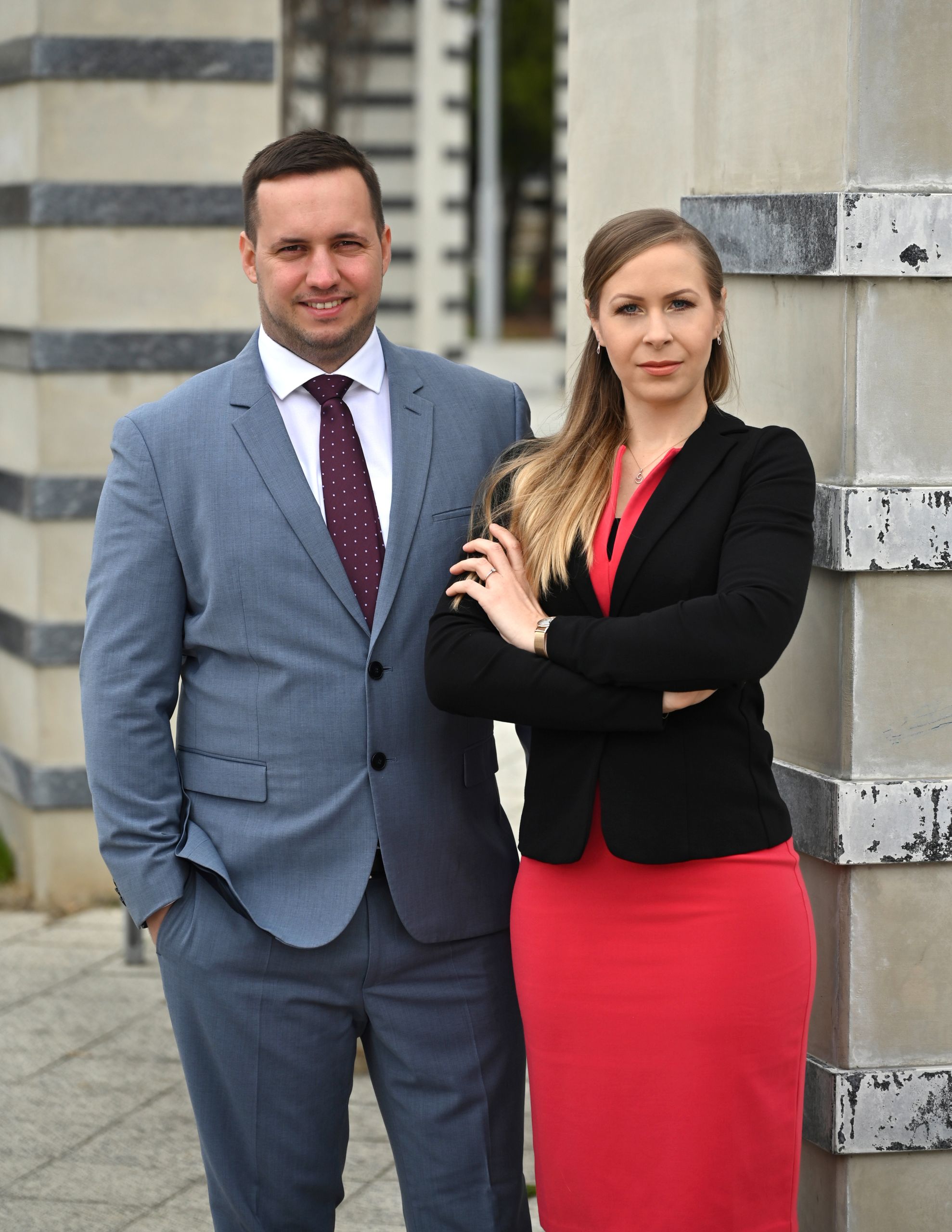 Selbstbewusstes Paar in Business-Kleidung posiert vor einem modernen Gebäude mit grauen und schwarzen Streifen