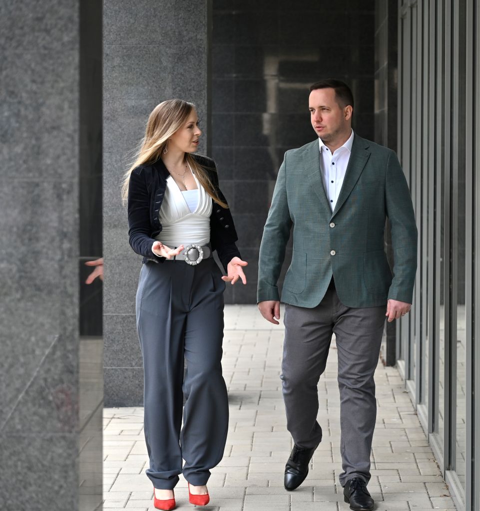 Mann und Frau führen ein intensives Gespräch beim Gehen entlang einer Glasfassade vor einem modernen Bürogebäude